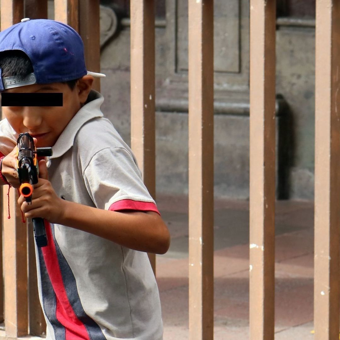Niño le apunta a fotógrafo con una pistola de plástico.