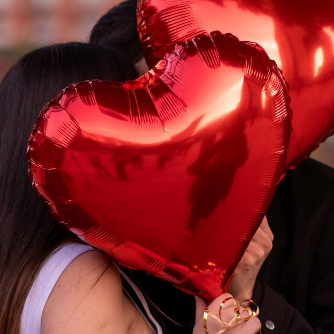 Pareja sostiene globos de corazones en el marco del Día del Amor y la Amistad