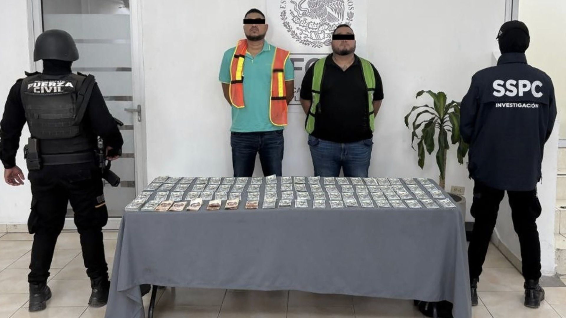 Oficiales flanquean a dos personas detenidas con 100 mil dólares en efectivo en Nuevo León