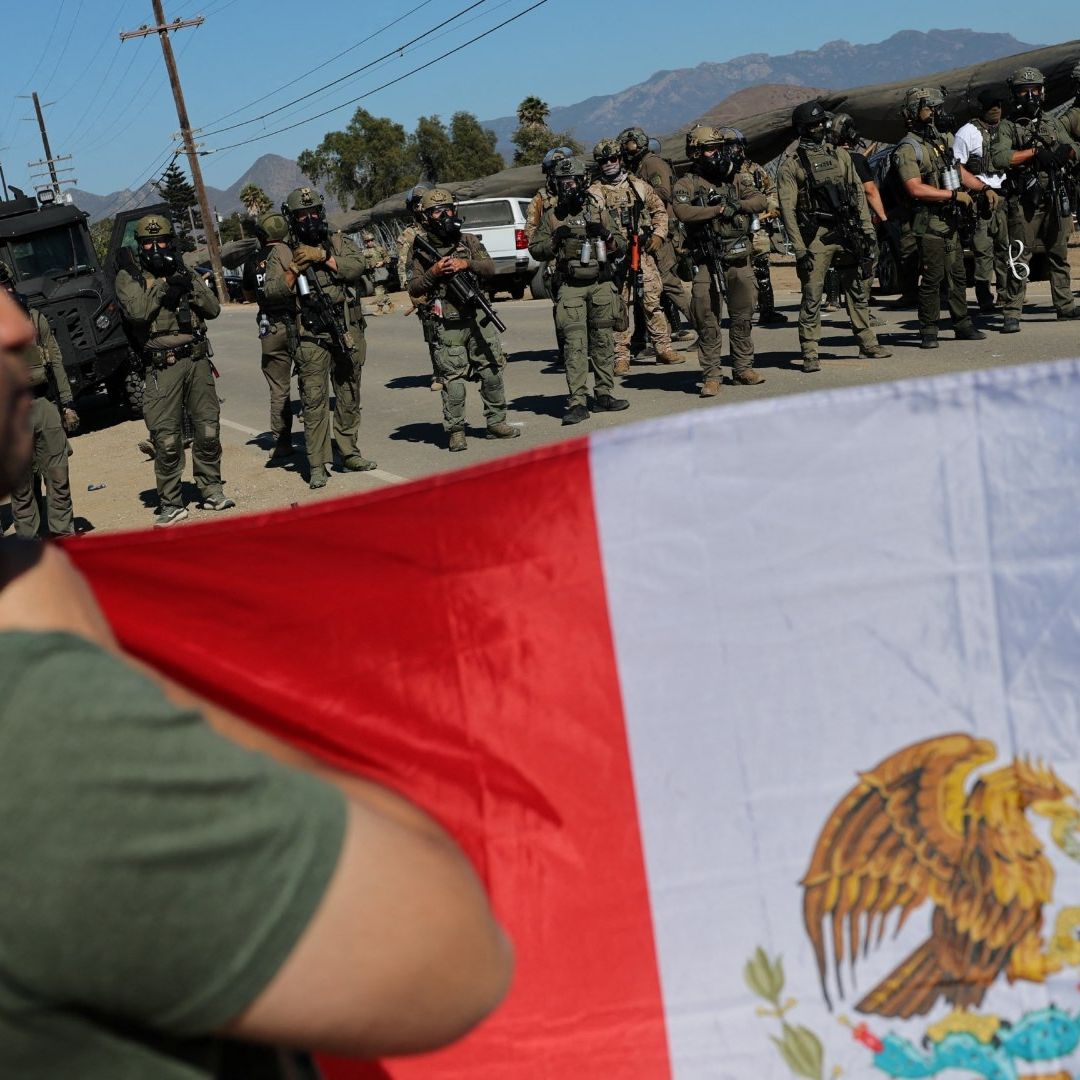 Personas muestran bandera de México frente a policías durante redada en California