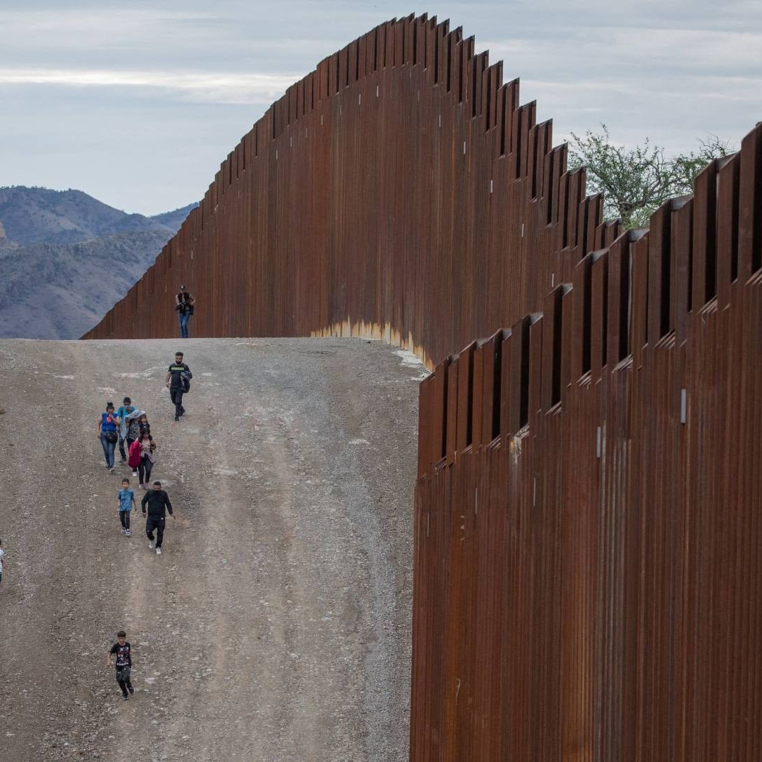 Migrantes caminan a lo largo del muro fronterizo en Ruby, Arizona, EUA,