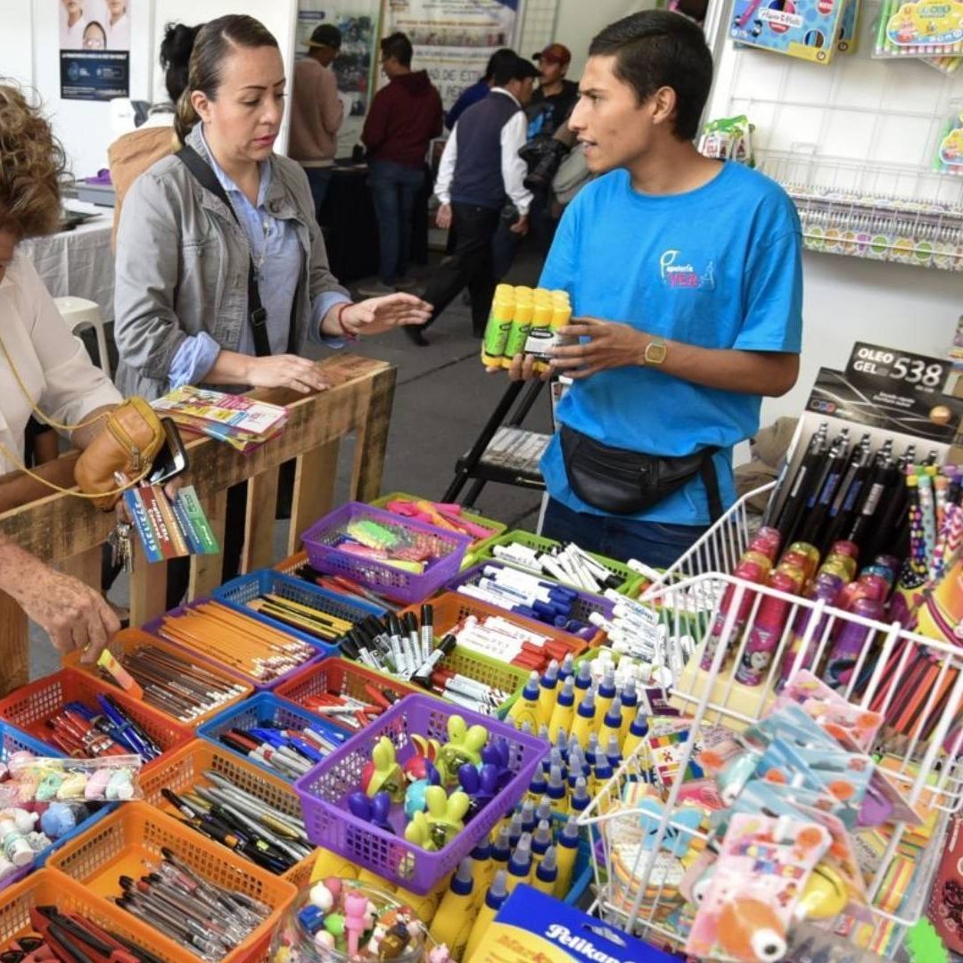 Mujer conversa con vendedor en puesto de venta de útiles escolares