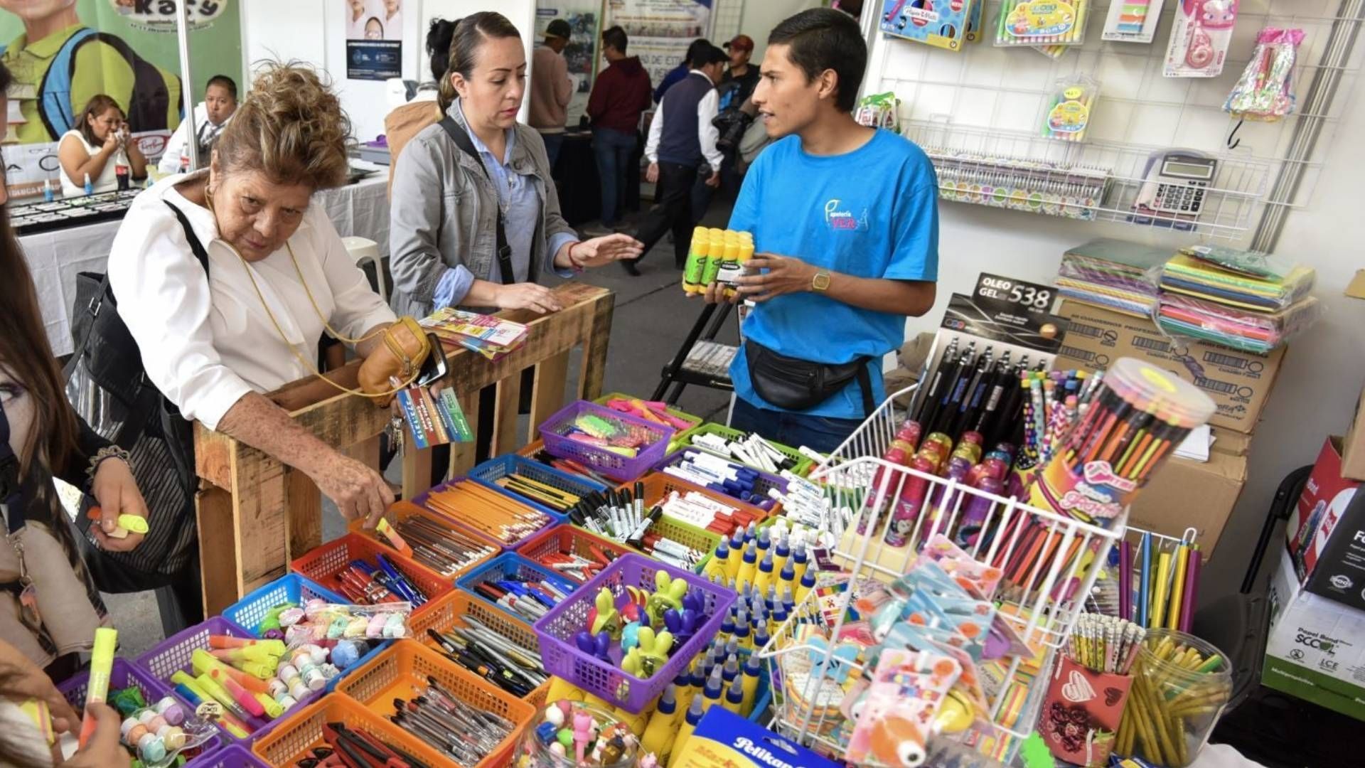 Mujer conversa con vendedor en puesto de venta de útiles escolares
