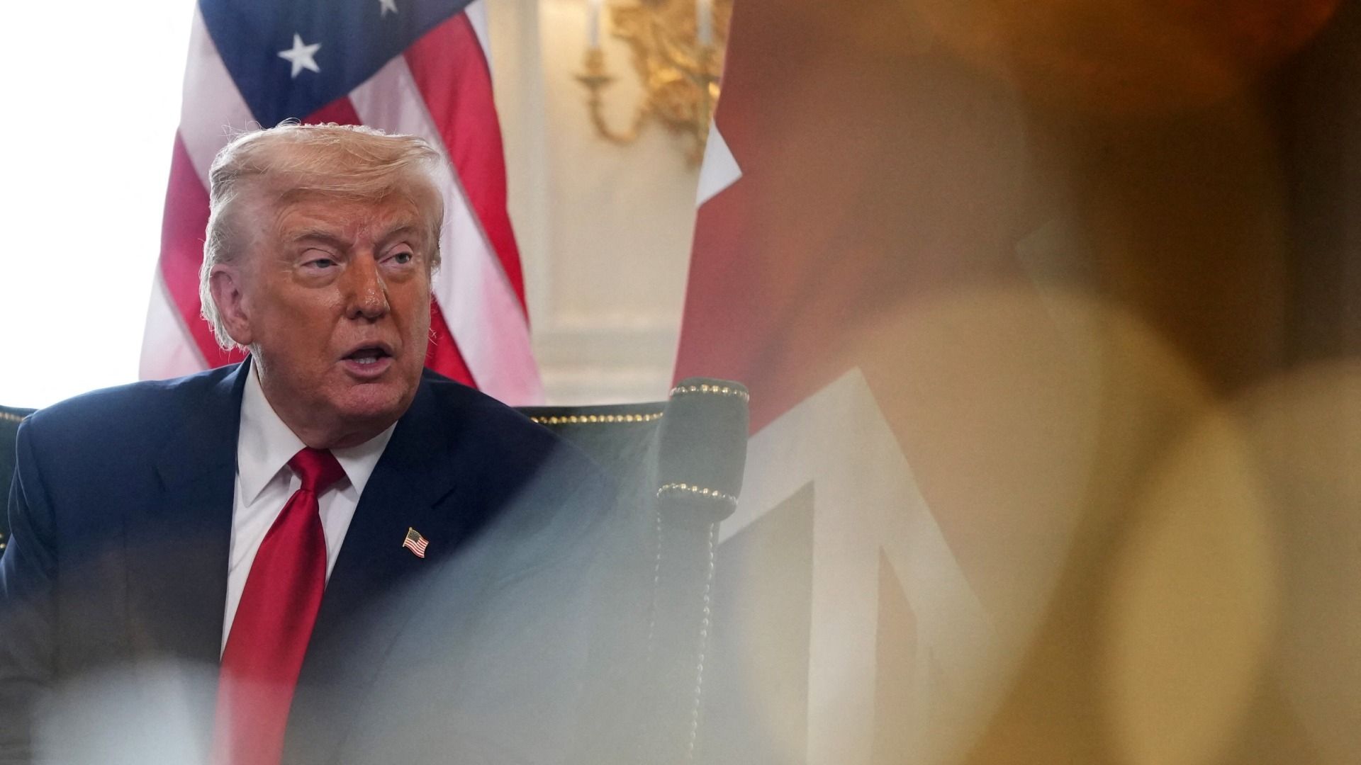 Donald Trump sentado y detrás de él una bandera de Estados Unidos