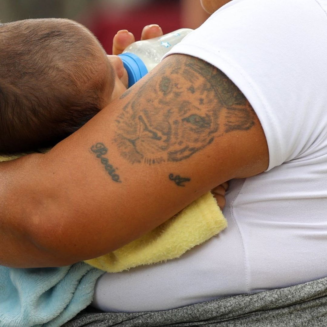 Mujer carga en brazos a bebé que toma leche de una mamila