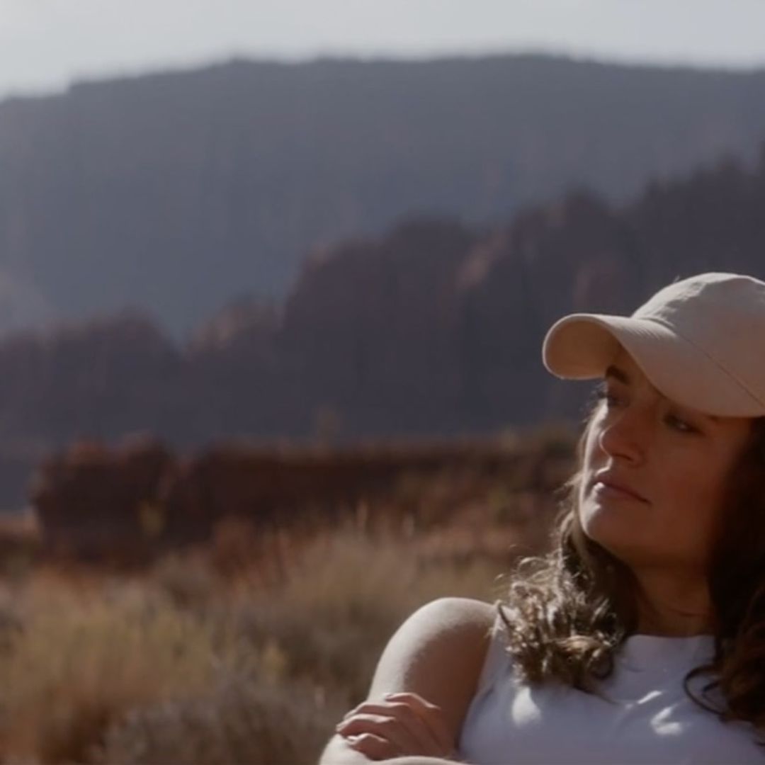 Una joven usa una gorra y observa un paisaje de áreas verdes.