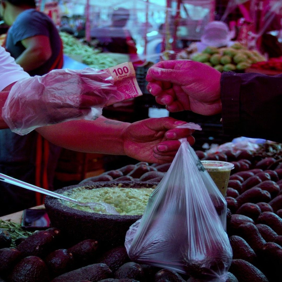 Una persona paga con billete de 100 pesos en un puesto de verduras.