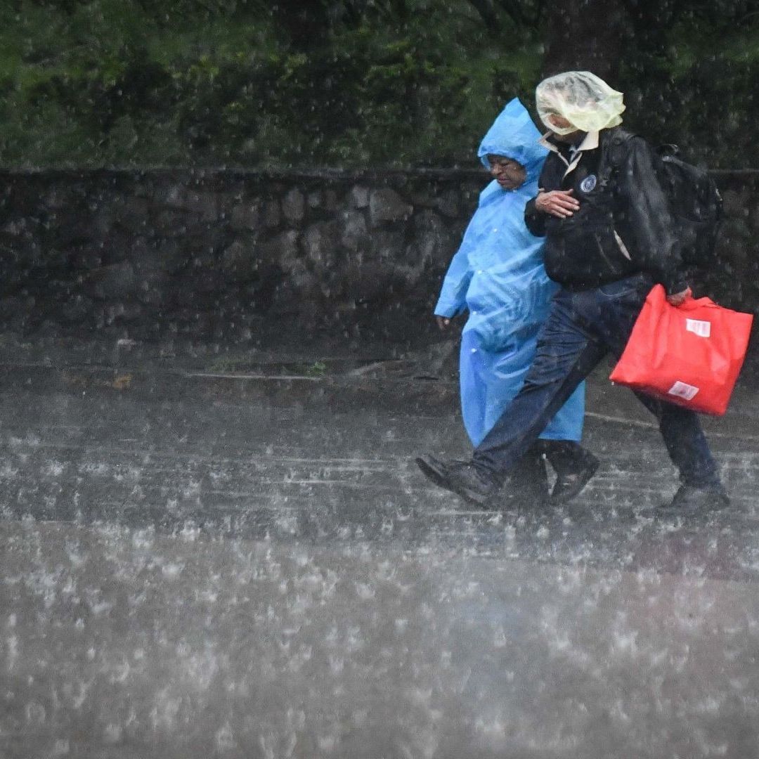 Dos personas usan un impermeable para cubrirse de la lluvia, mientras curzan la calle.
