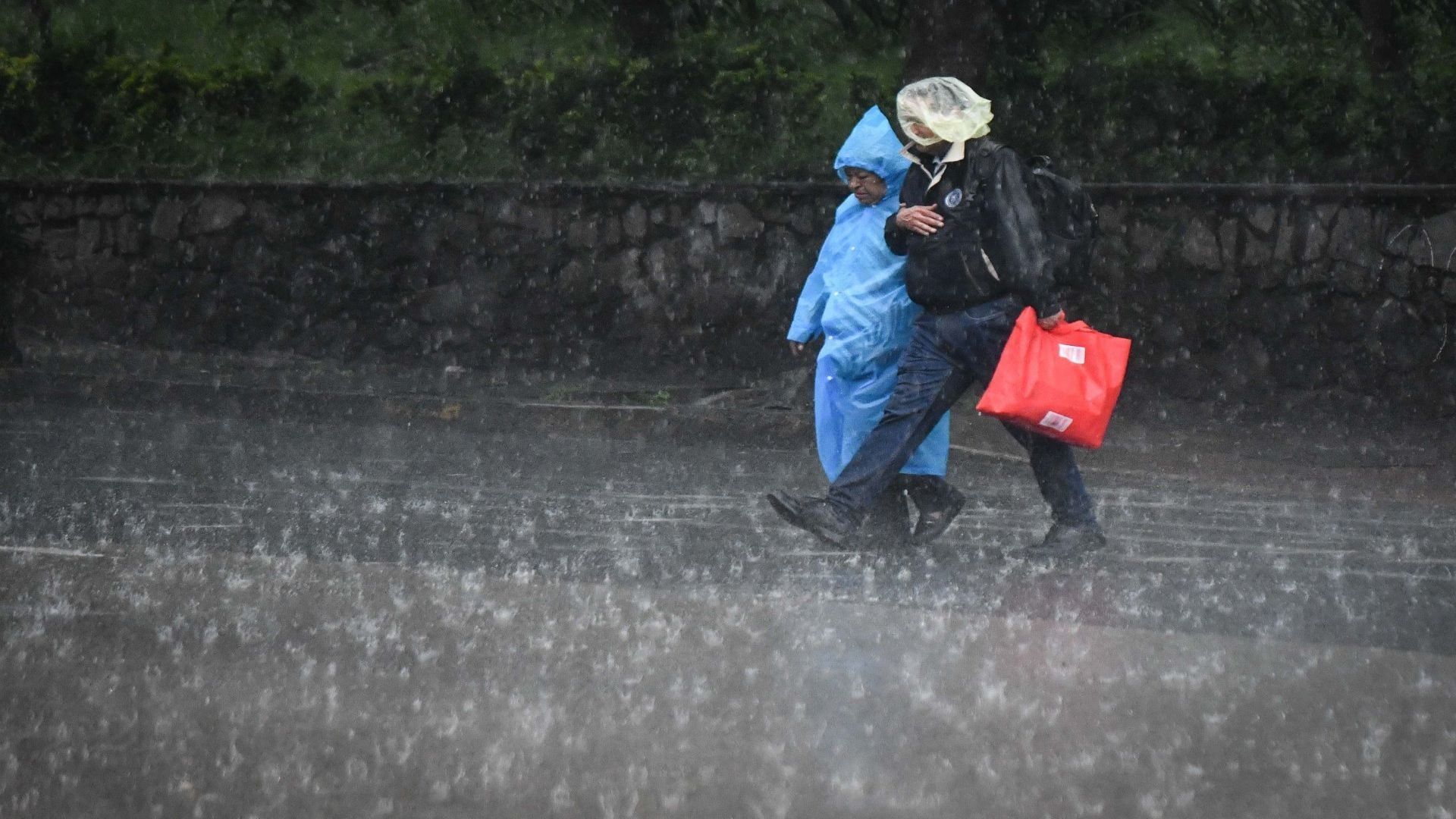 Dos personas usan un impermeable para cubrirse de la lluvia, mientras curzan la calle.
