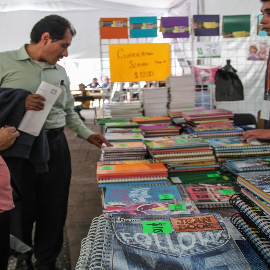 Una mujer y un hombre comprando útiles escolares; hay cuadernos de colores.