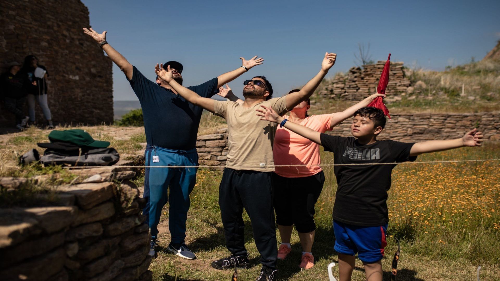 Cuatro personas se encuentran en un espacio verde, expandiendo lo brazos y volteando hacia el cielo.