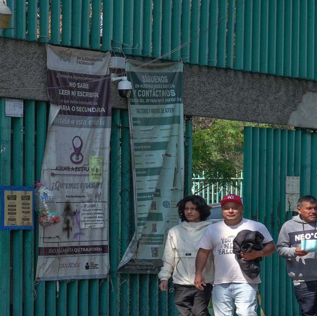 En la imagen se puede ver una escuela de color verde, enfrente pasa un joven y dos adultos.