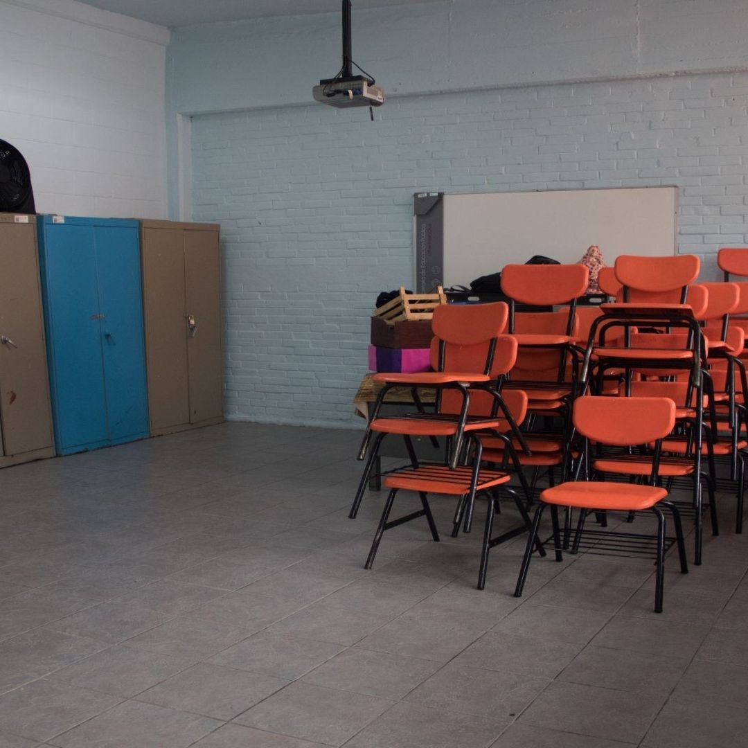 Varias sillas de color naranja amontonadas en un salón de clases vacio.