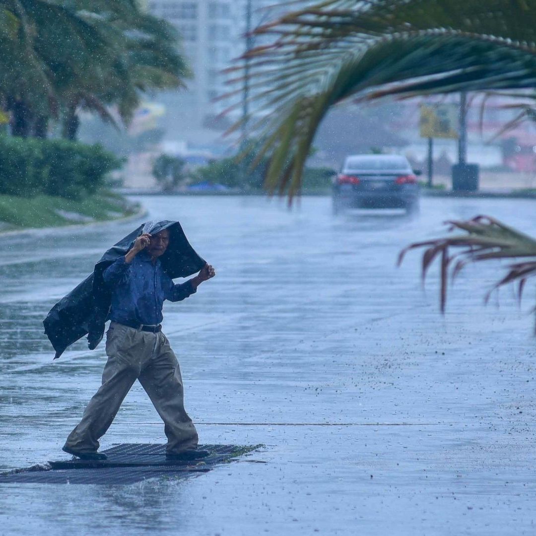 Un hombre de la tercera edad cruza la calle mientras llueve; se cubre con una bolsa.