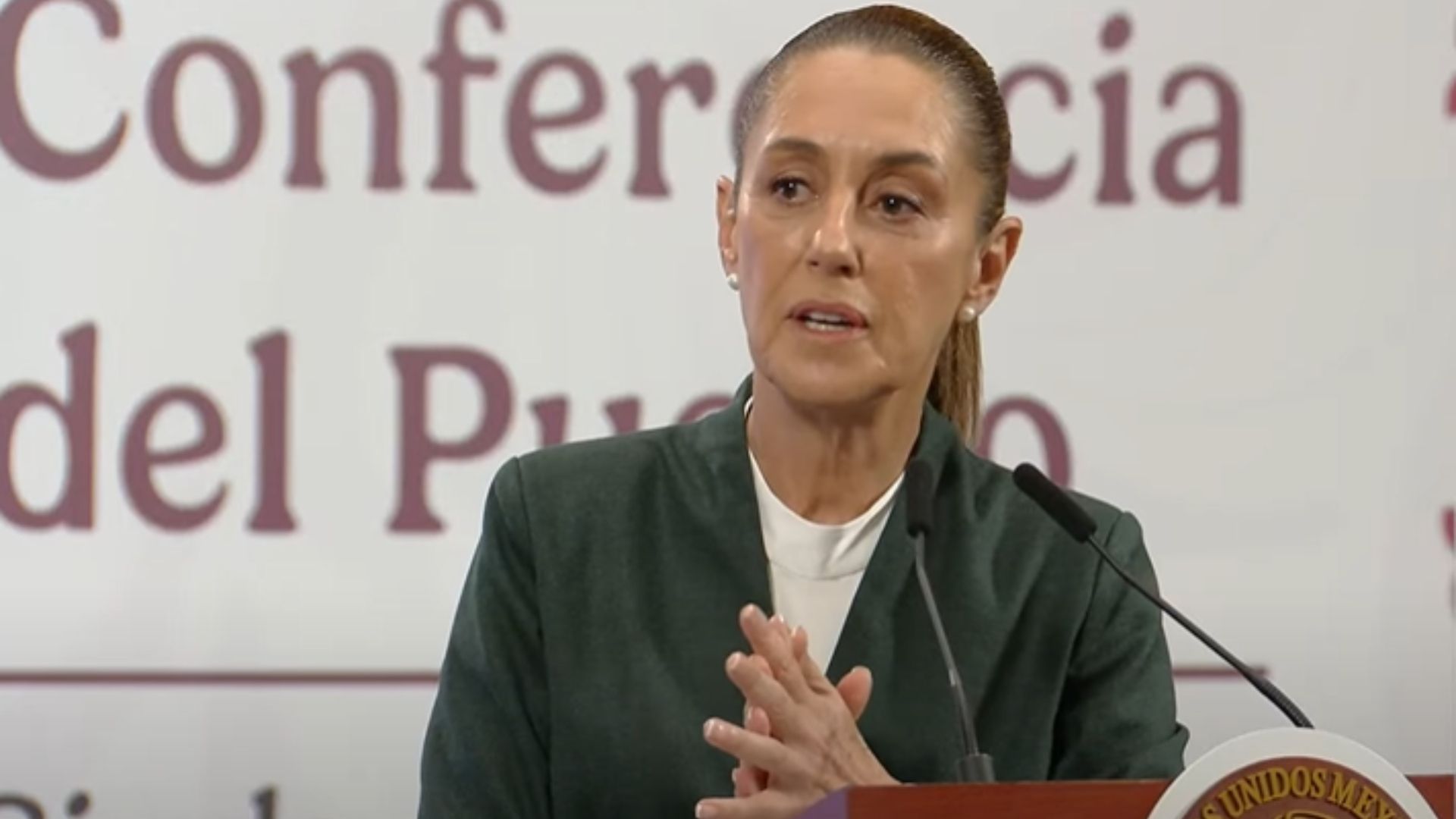 Una mujer viste de color verde con blanco, atrás hay unas letras.