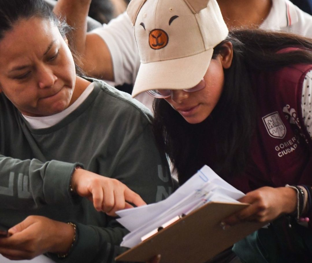 Una trabajadora con gorra de capibara da una hoja blanca a una mujer.
