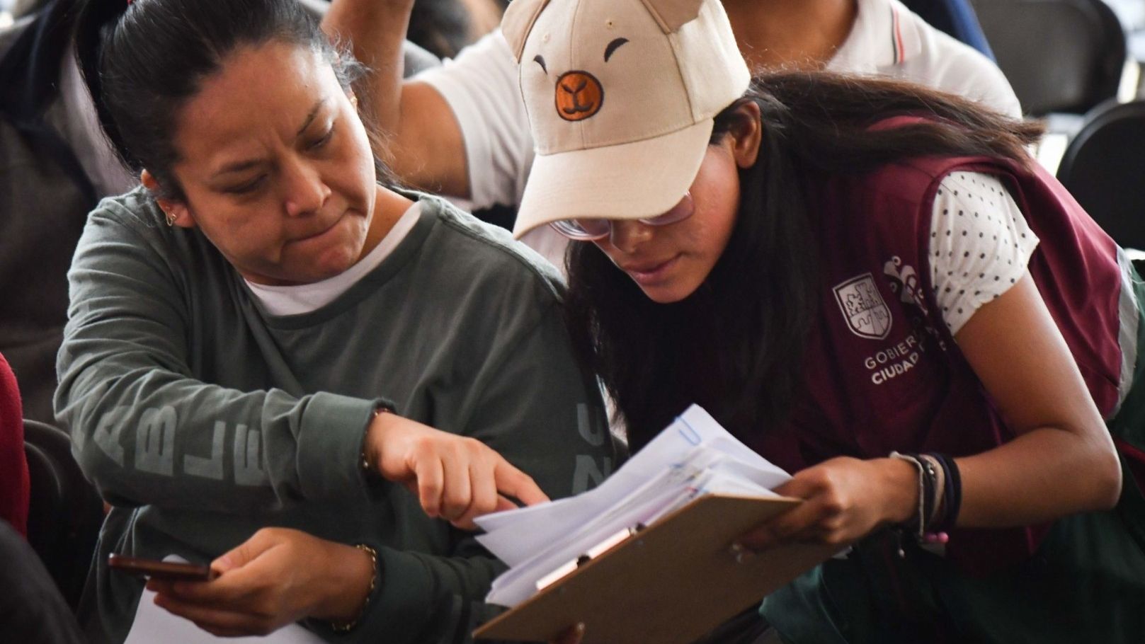 Una trabajadora con gorra de capibara da una hoja  blanca a una mujer.