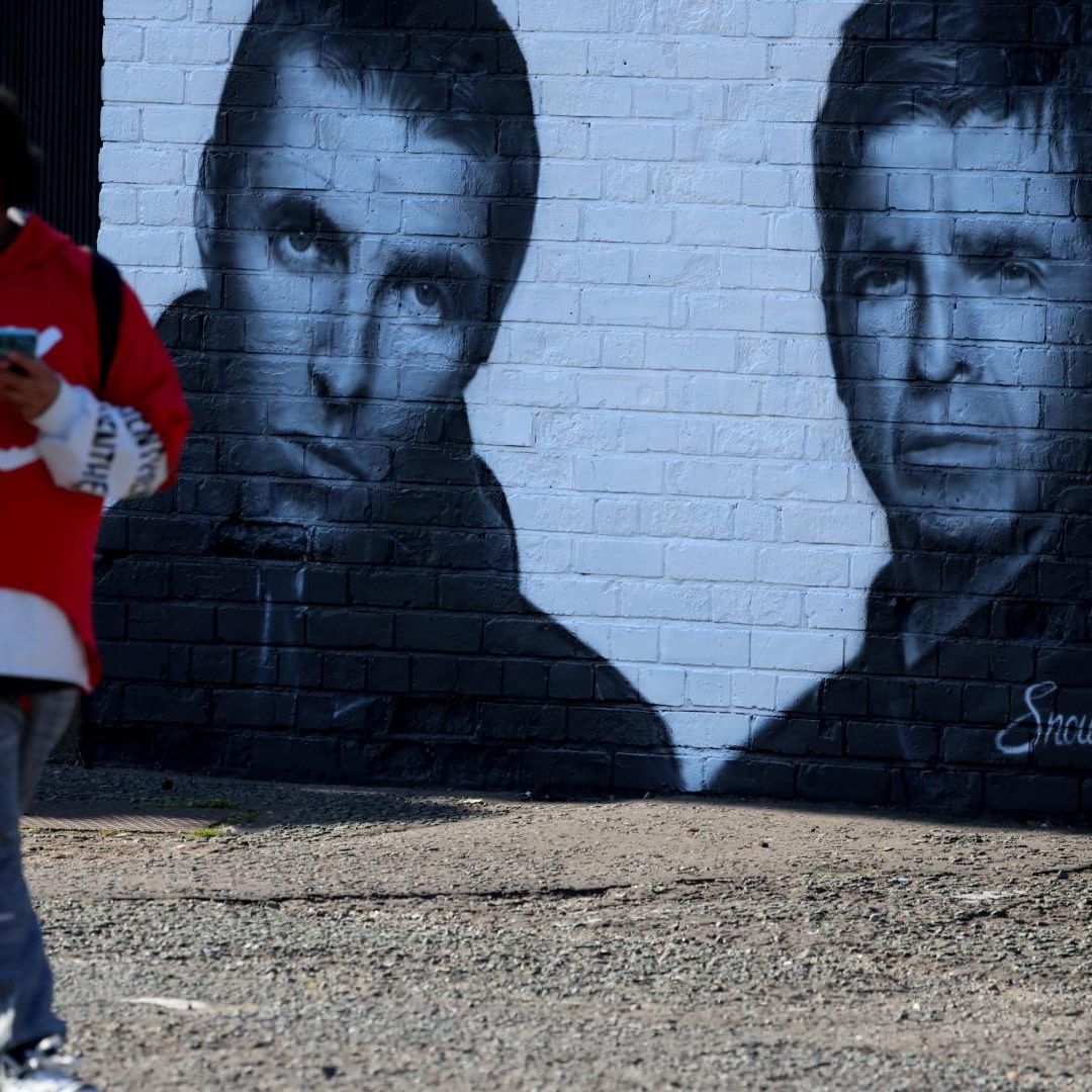 Un hombre pasa junto a un mural de los miembros de la banda Oasis