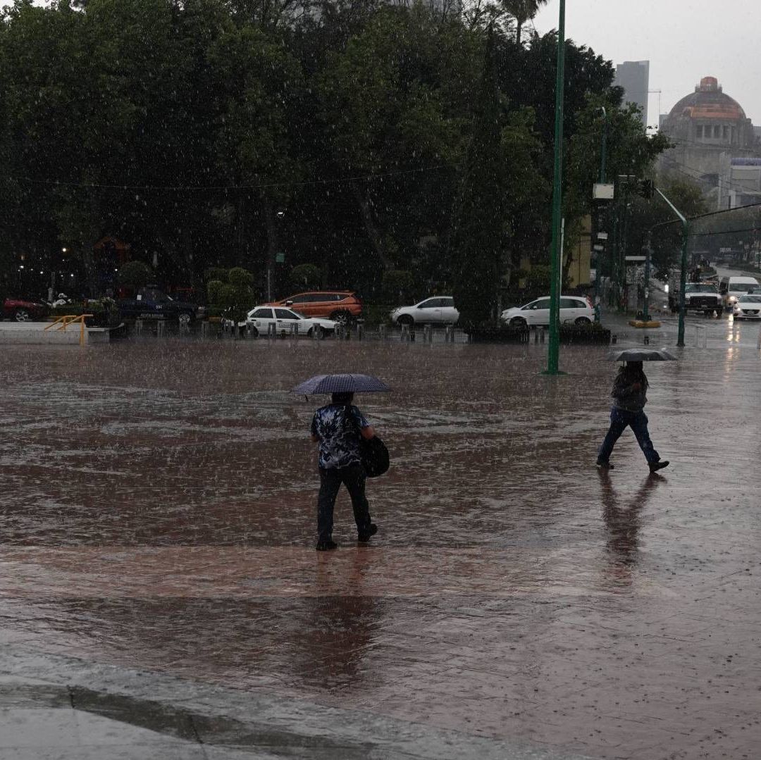 Tres personas cruzan la calle en medio de fuertes lluvias.