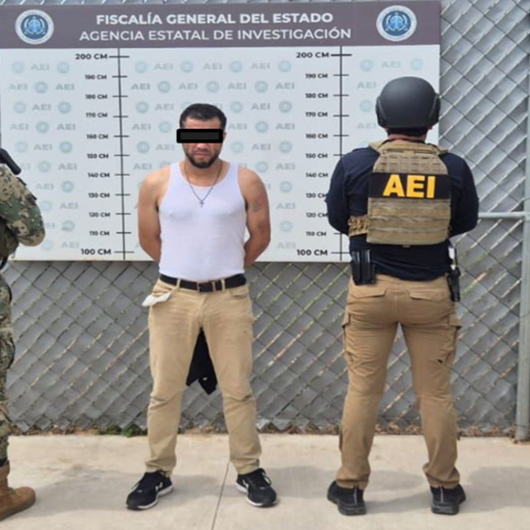 Un hombre vestido de blanco y gris está en medio de elementos del Ejército, quienes lo resguardad.