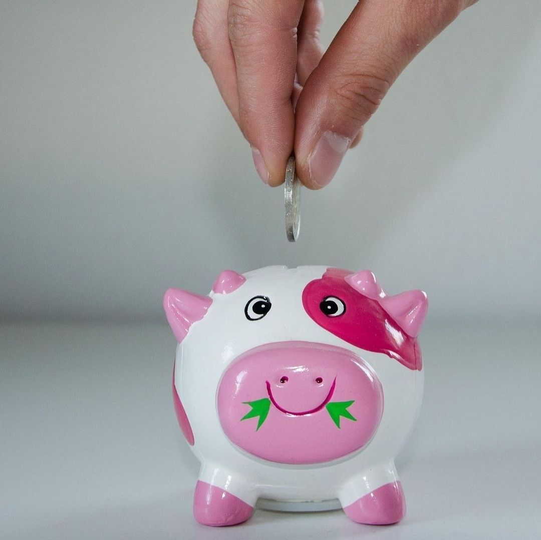 Una alcancía de puerquito de color rosa, una mano deposita una moneda.