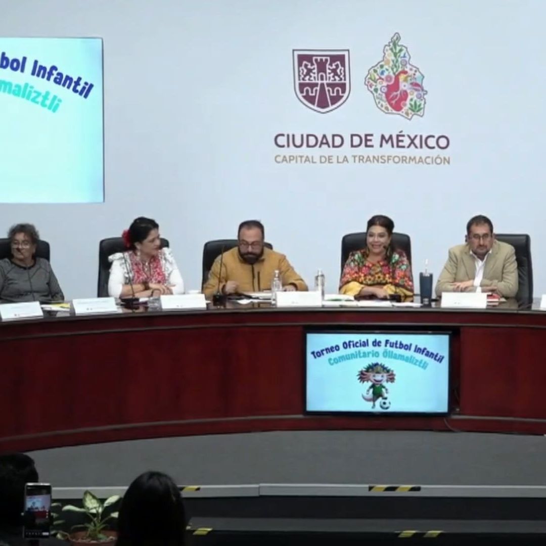 Varias personas en una mesa, hablan en micrófono.
