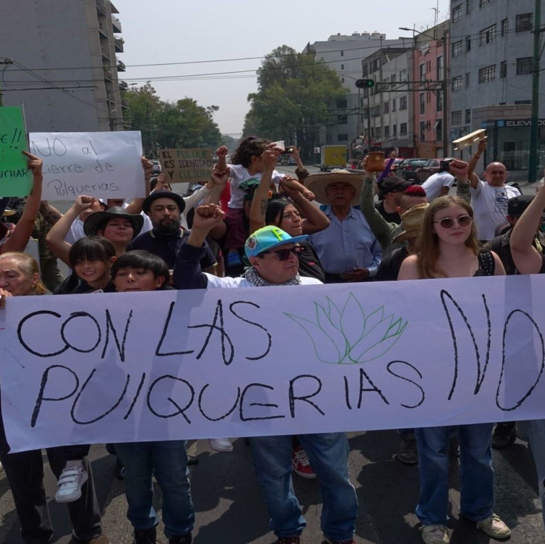 Varias personas reunidas para marchar llevan un cartel que dice "Con las Pulquerías no".