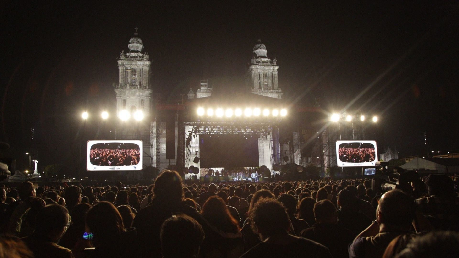 Varias personas reunidas en un concierto, hay pantallas y luces.