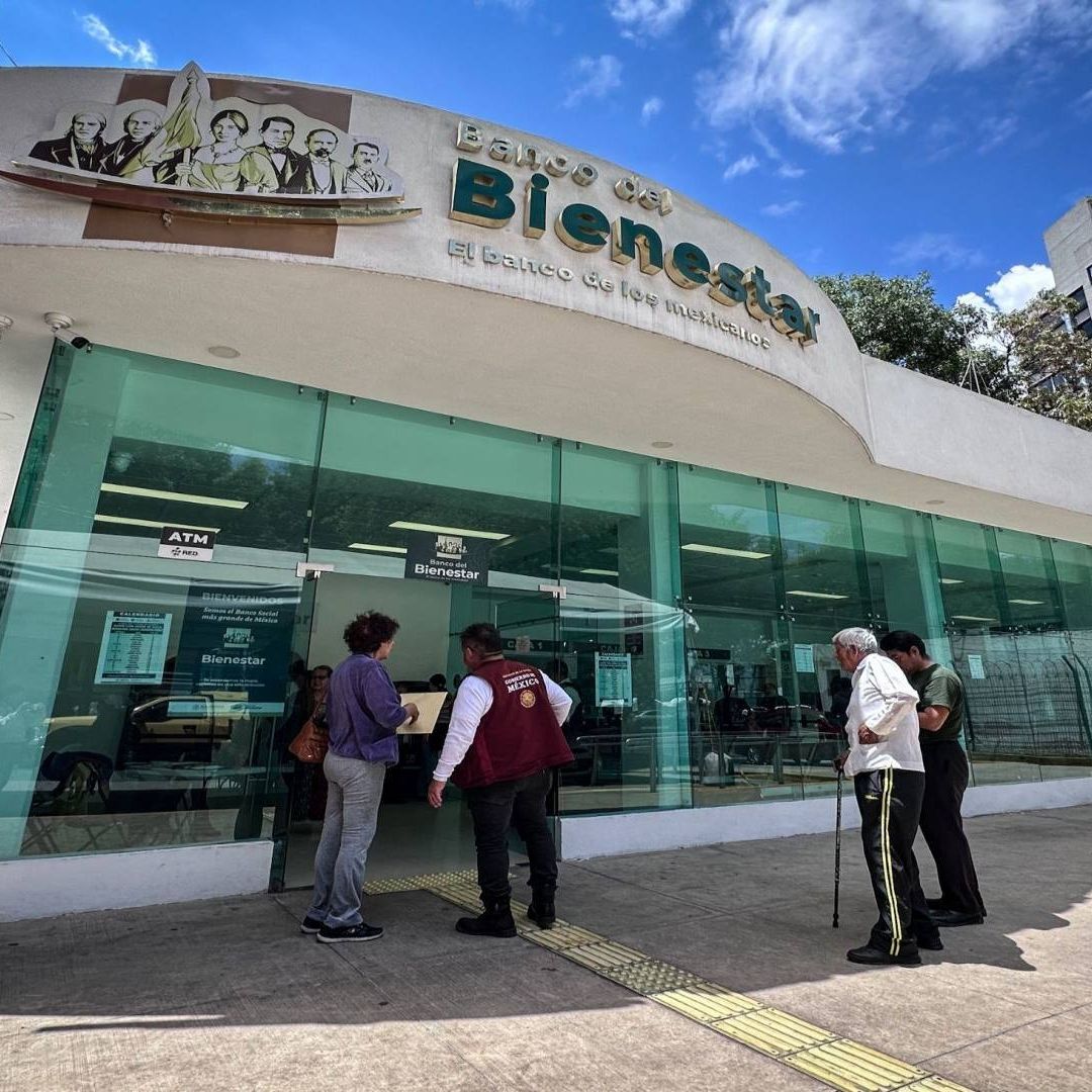Un banco de color blanco con puertas de cristal grandes, un par de personas están por entrar.
