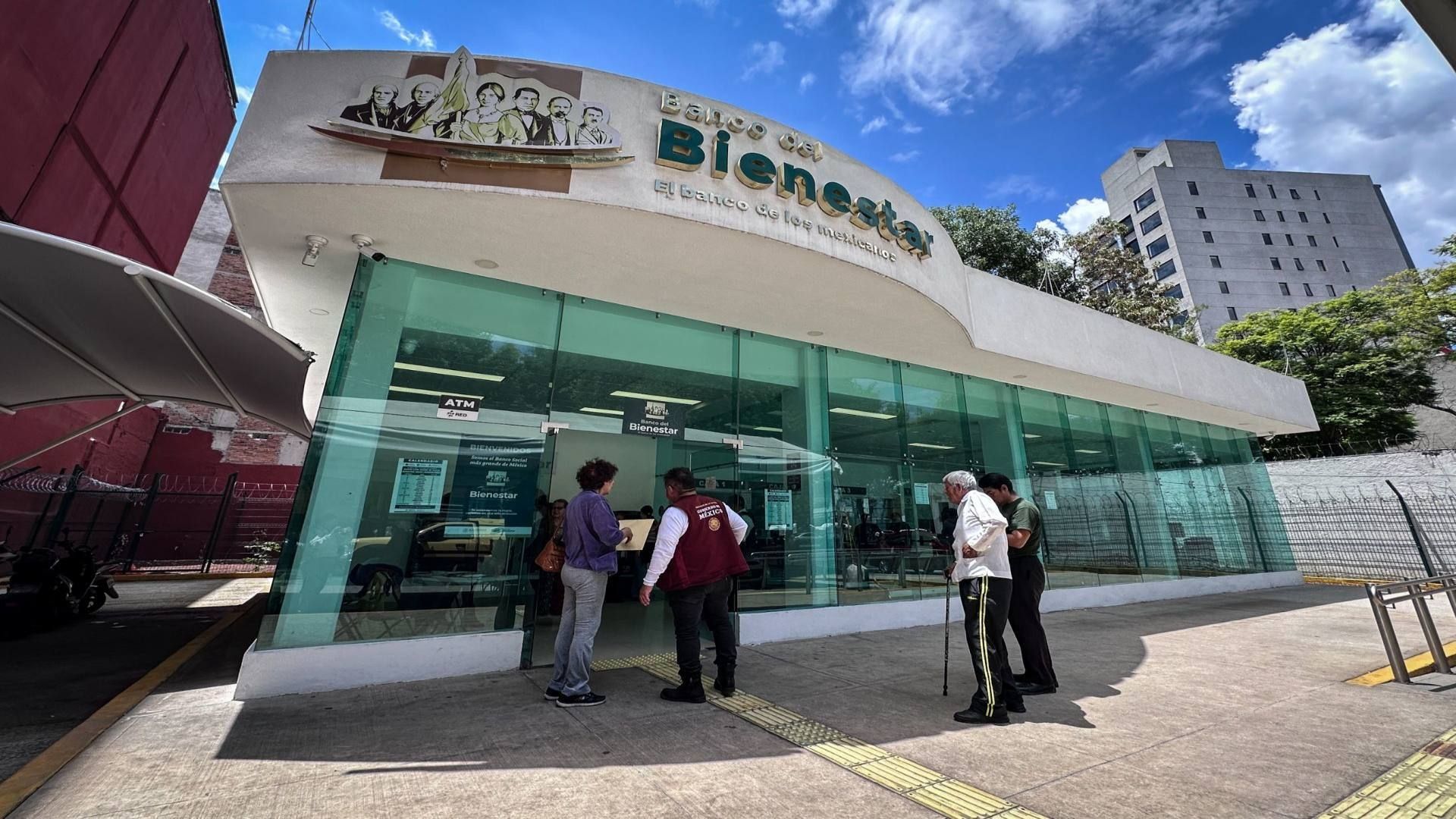 Un banco de color blanco con puertas de cristal grandes, un par de personas están por entrar.