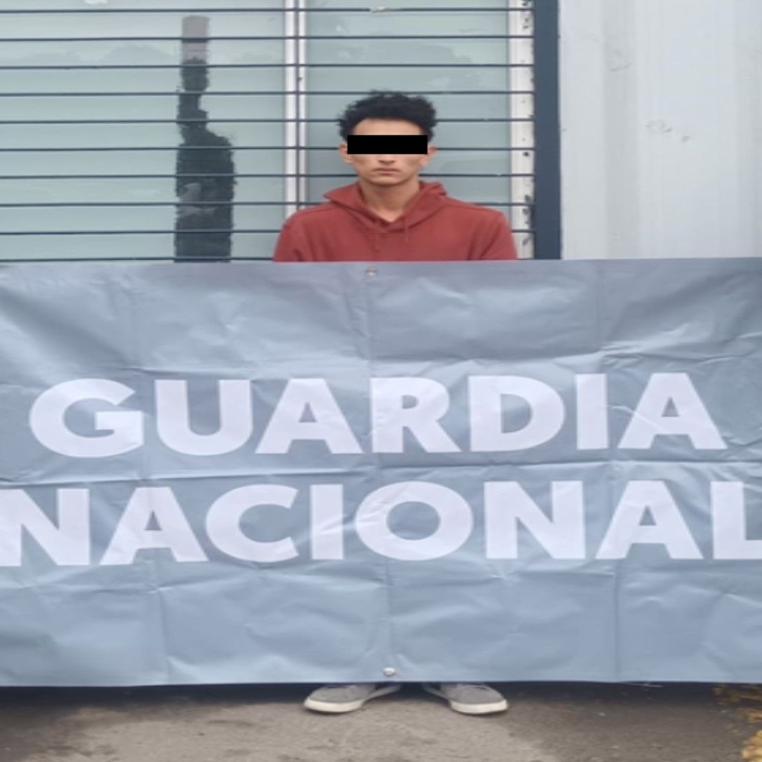 Un hombre con los ojos tapados, con una lona que dice "Guardia Nacional".