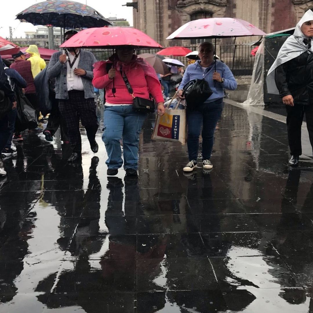 Varias personas caminan en la calle tapadas con sombrillas por las lluvias.