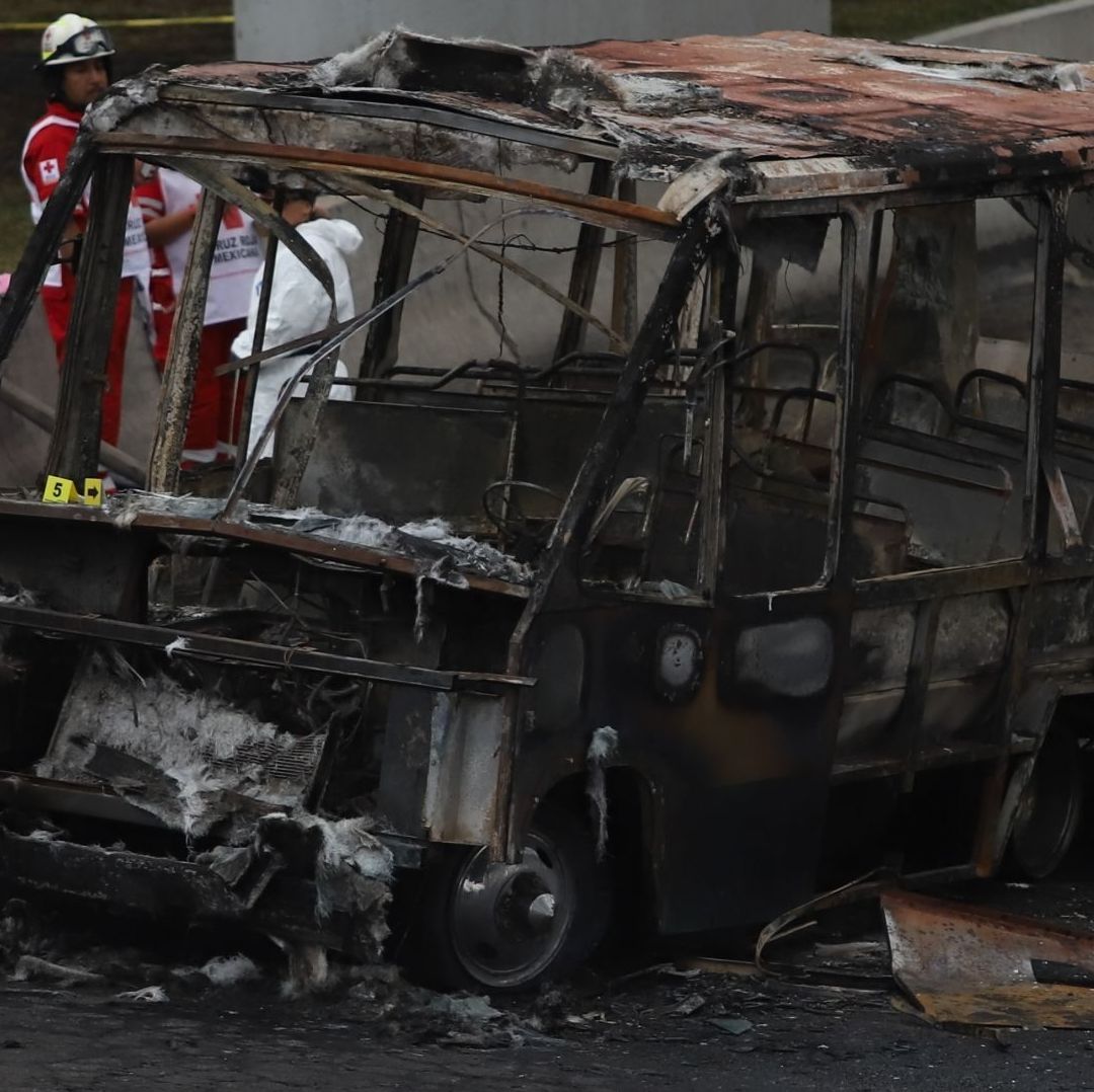 Un bombero con un traje naranja, enfrente de un vehículo dañado.