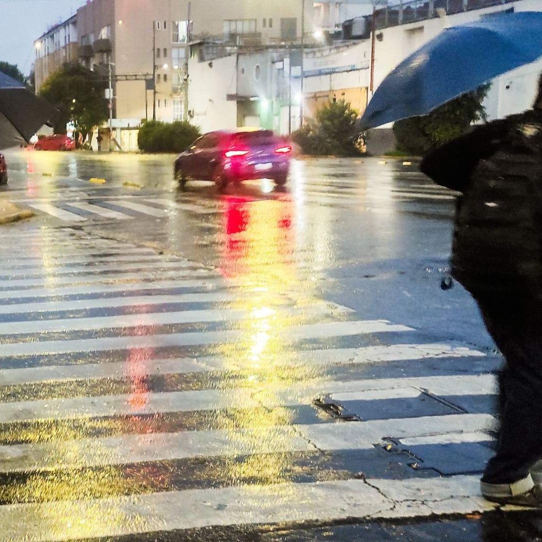 Dos hombres con sombrilla cruzan la calle.
