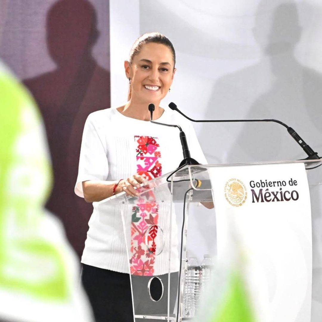 Una mujer vestida de blanco, habla en micrófono.
