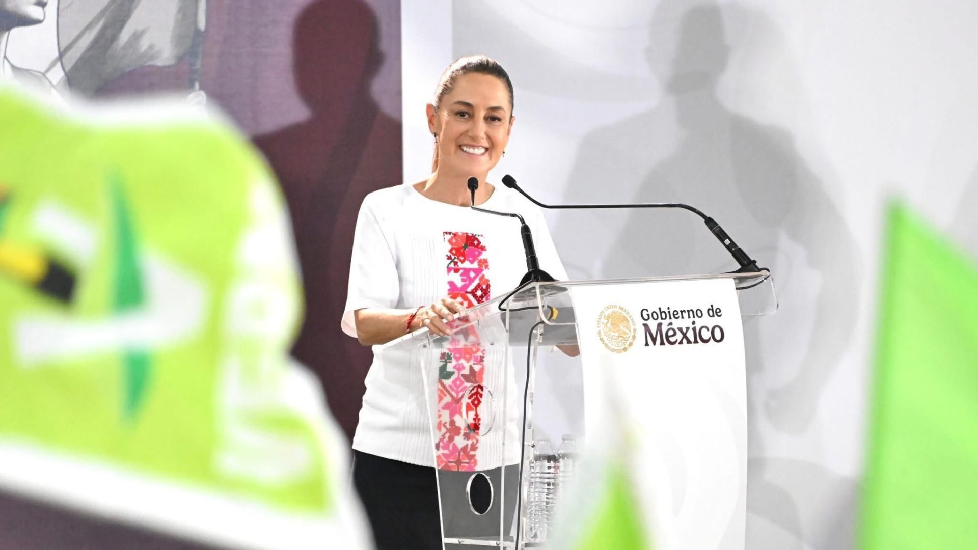 Una mujer vestida de blanco, habla en micrófono.