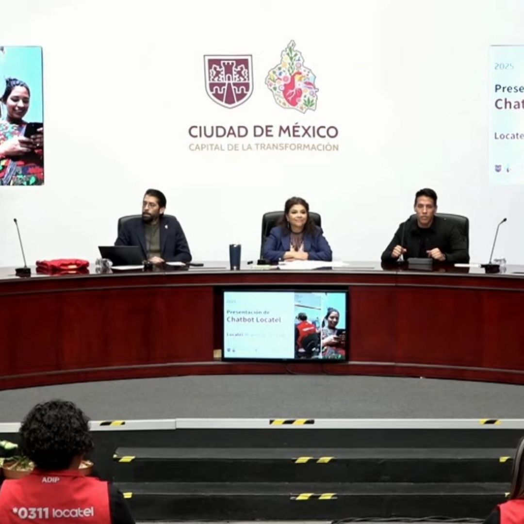 Una conferencia de prensa. Hay personas en una mesa y detrás una pantalla.