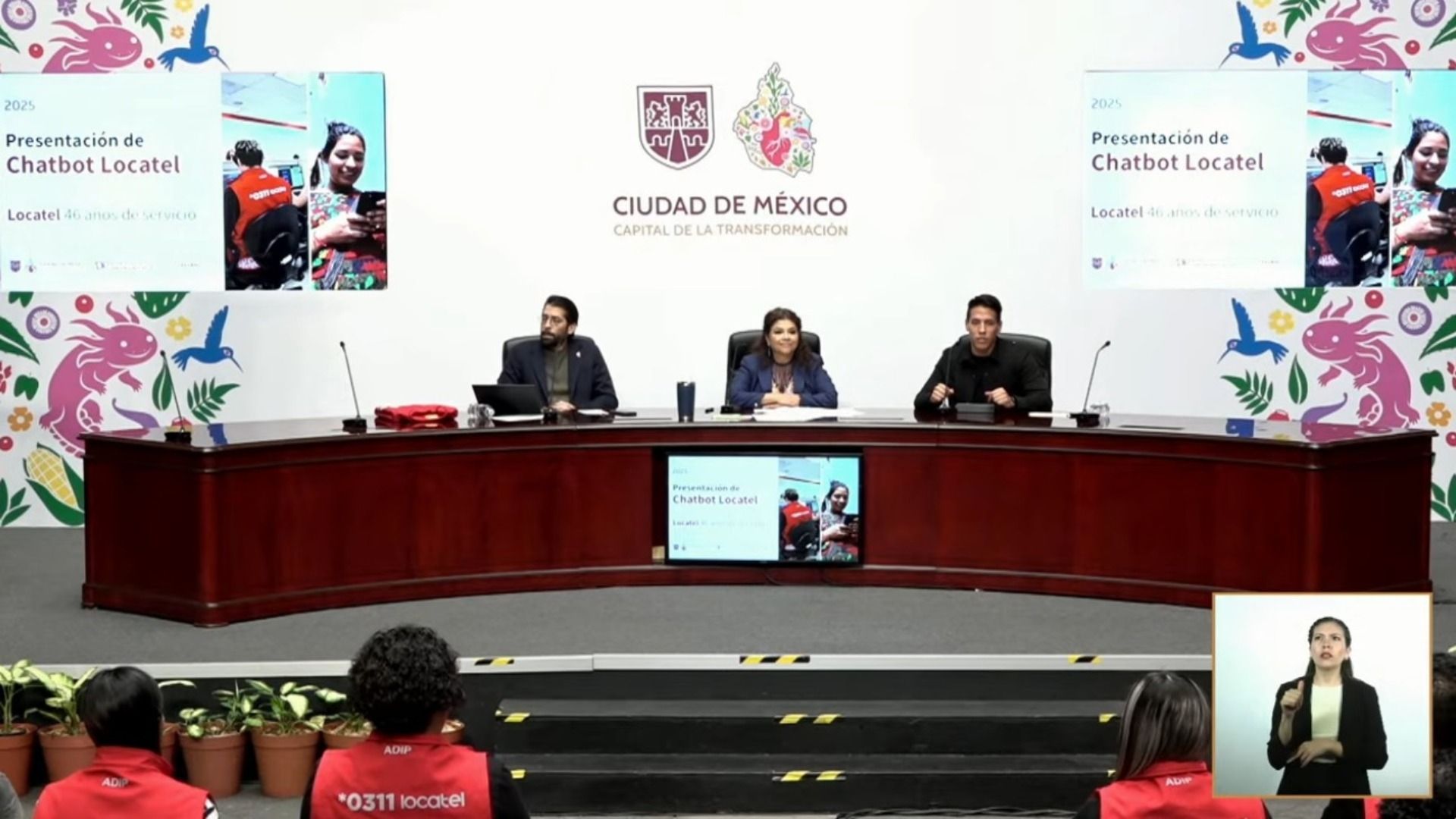 Una conferencia de prensa. Hay personas en una mesa y detrás una pantalla.