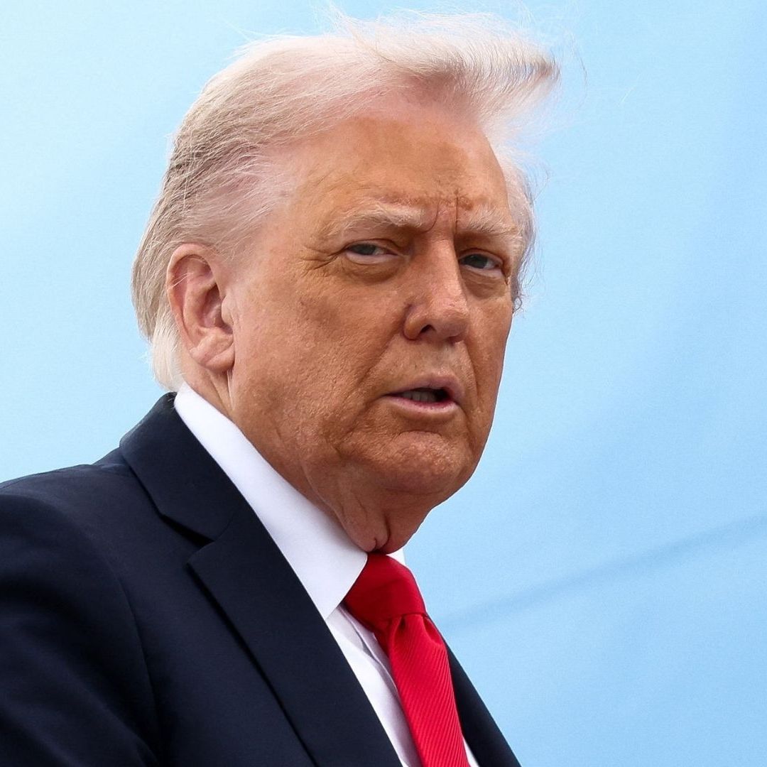 Un hombre con cabello con canas viste un traje negro con corbata roja.