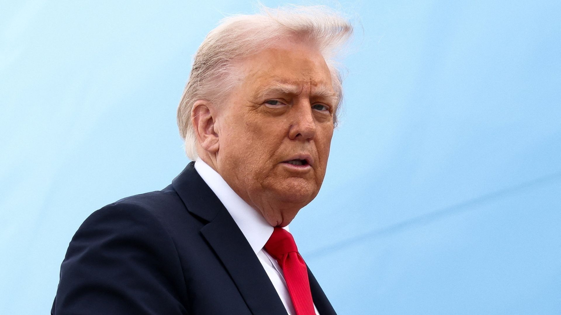 Un hombre con cabello con canas viste un traje negro con corbata roja.