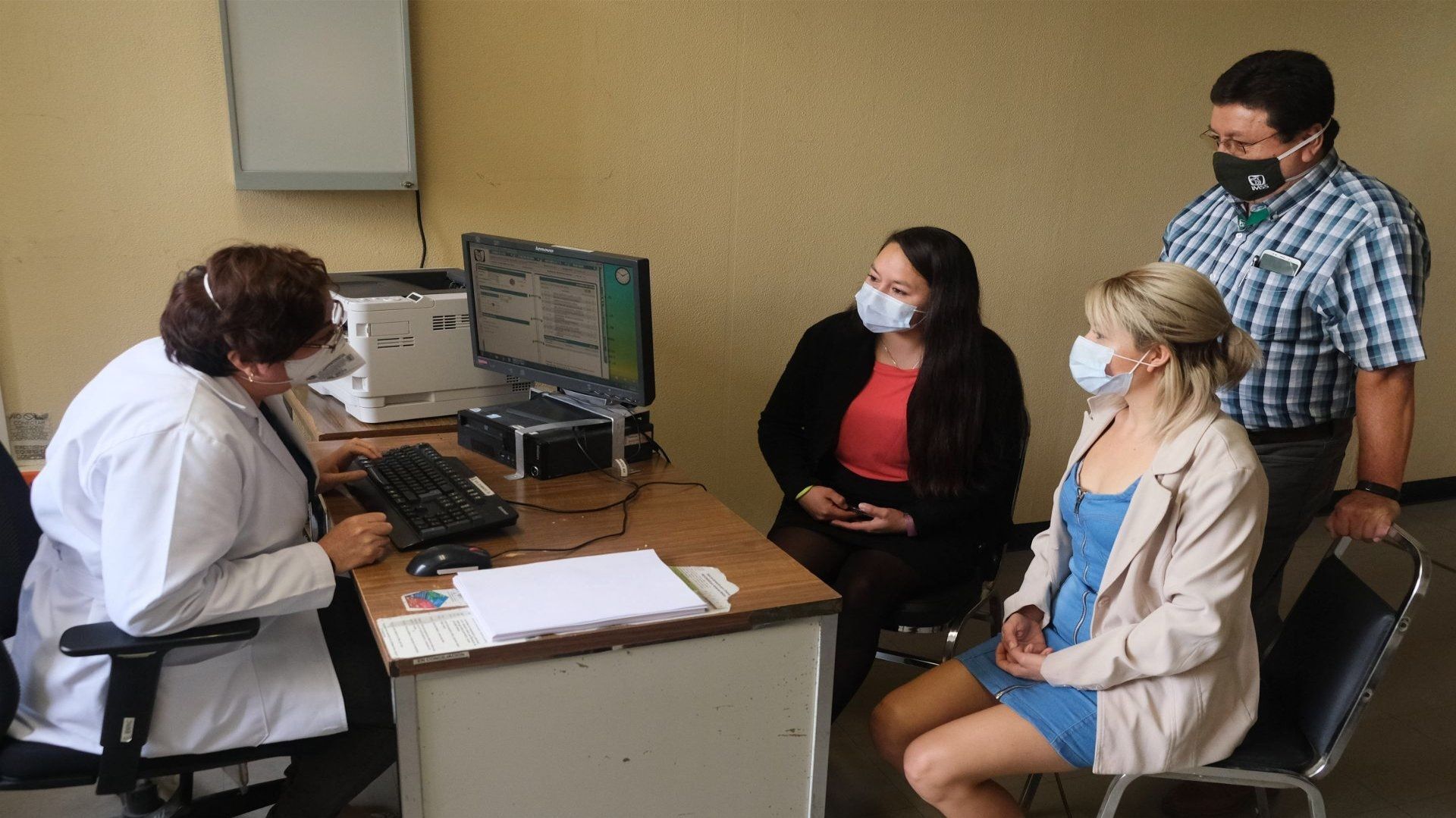 Tres personas frente a una doctora reciben en un consultorio médico.