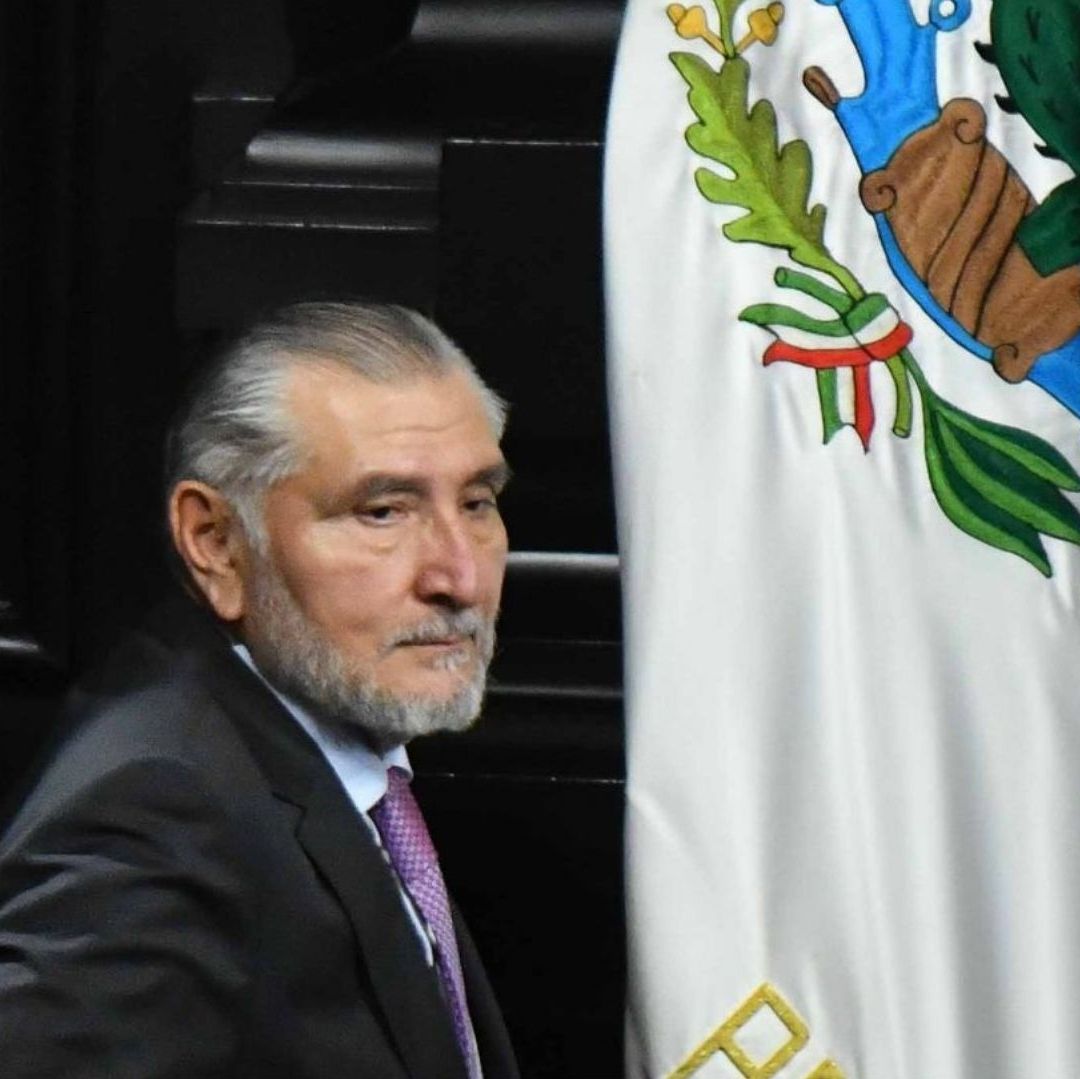 Un hombre frente a la bandera de México tiene un semblante triste.