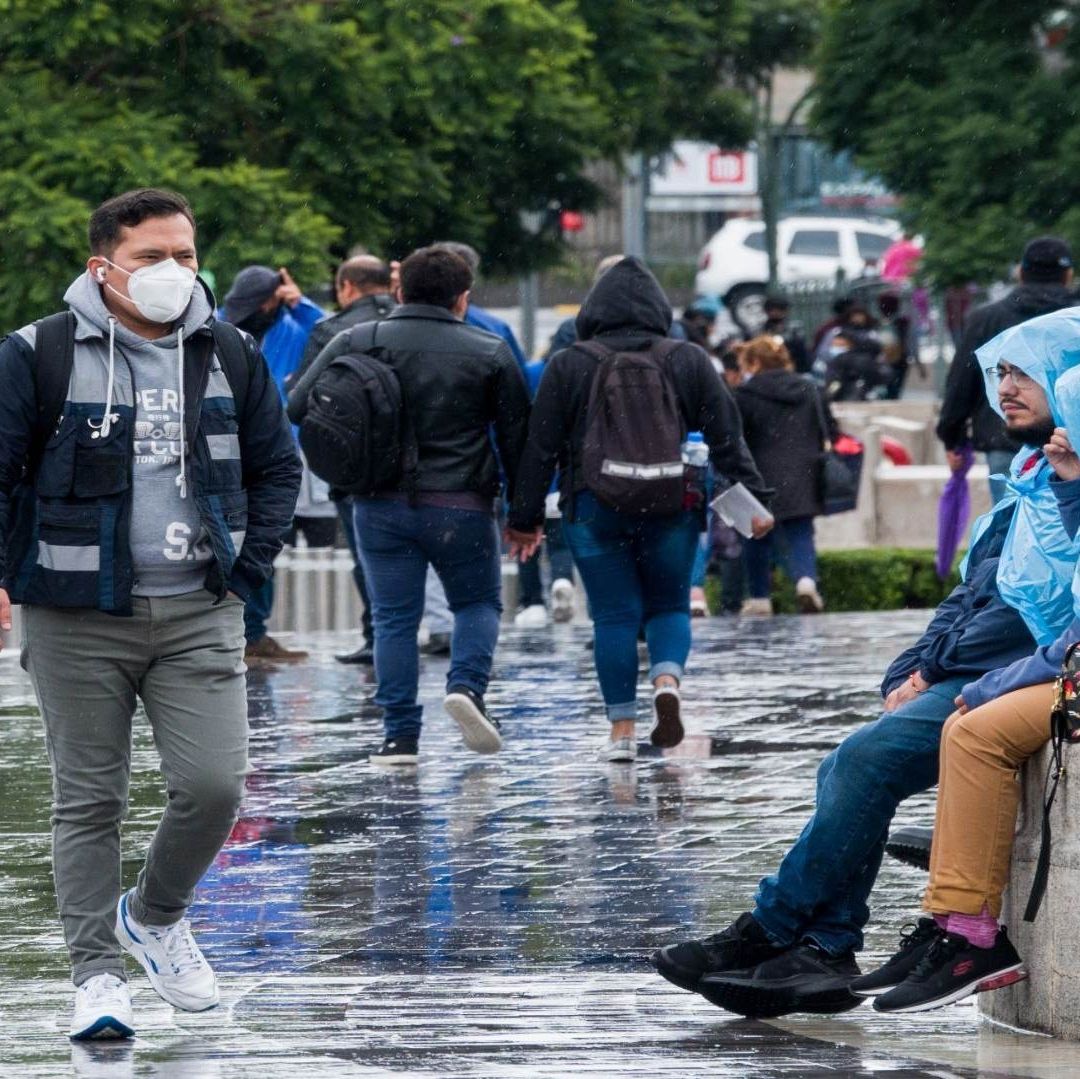 Varias personas sentadas se cubren de la lluvia.