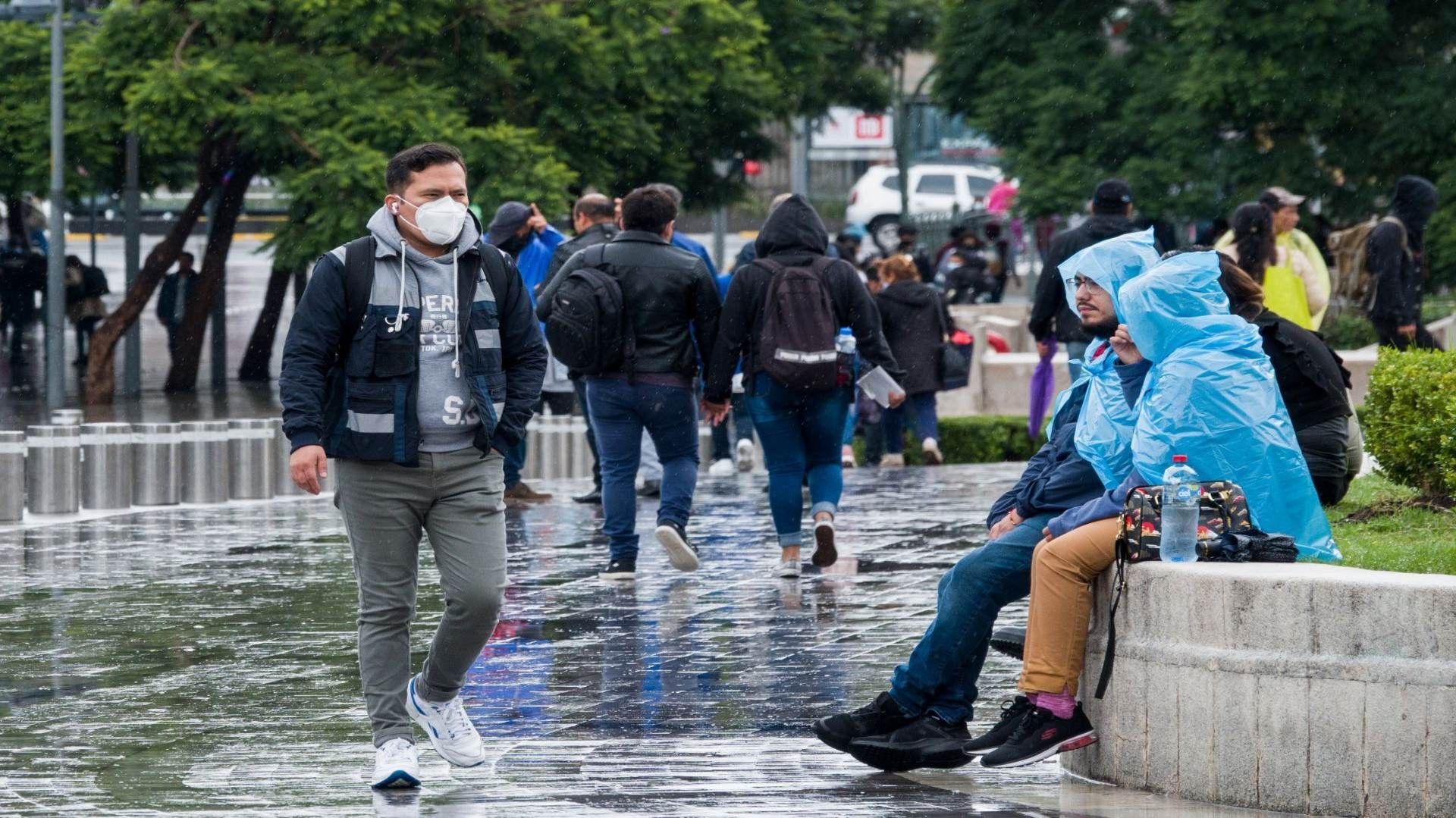 Varias personas sentadas se cubren de la lluvia.