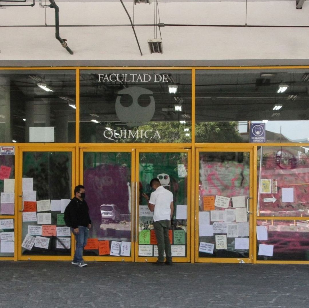 Una imagen de una escuela con carteles, hay dos estudiantes frente a ellos.