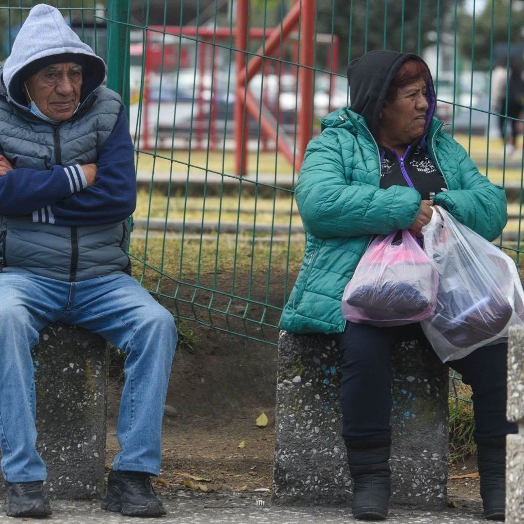 Dos personas abrigadas están sentadas en la banca de un parque.
