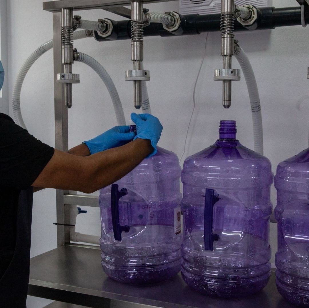 Un hombre llena garrafones morados con agua.