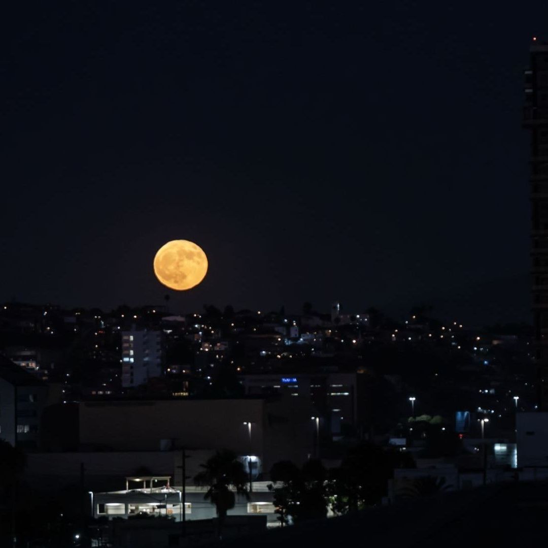 La superluna luce muy brillante en medio de un paisaje con edificios.