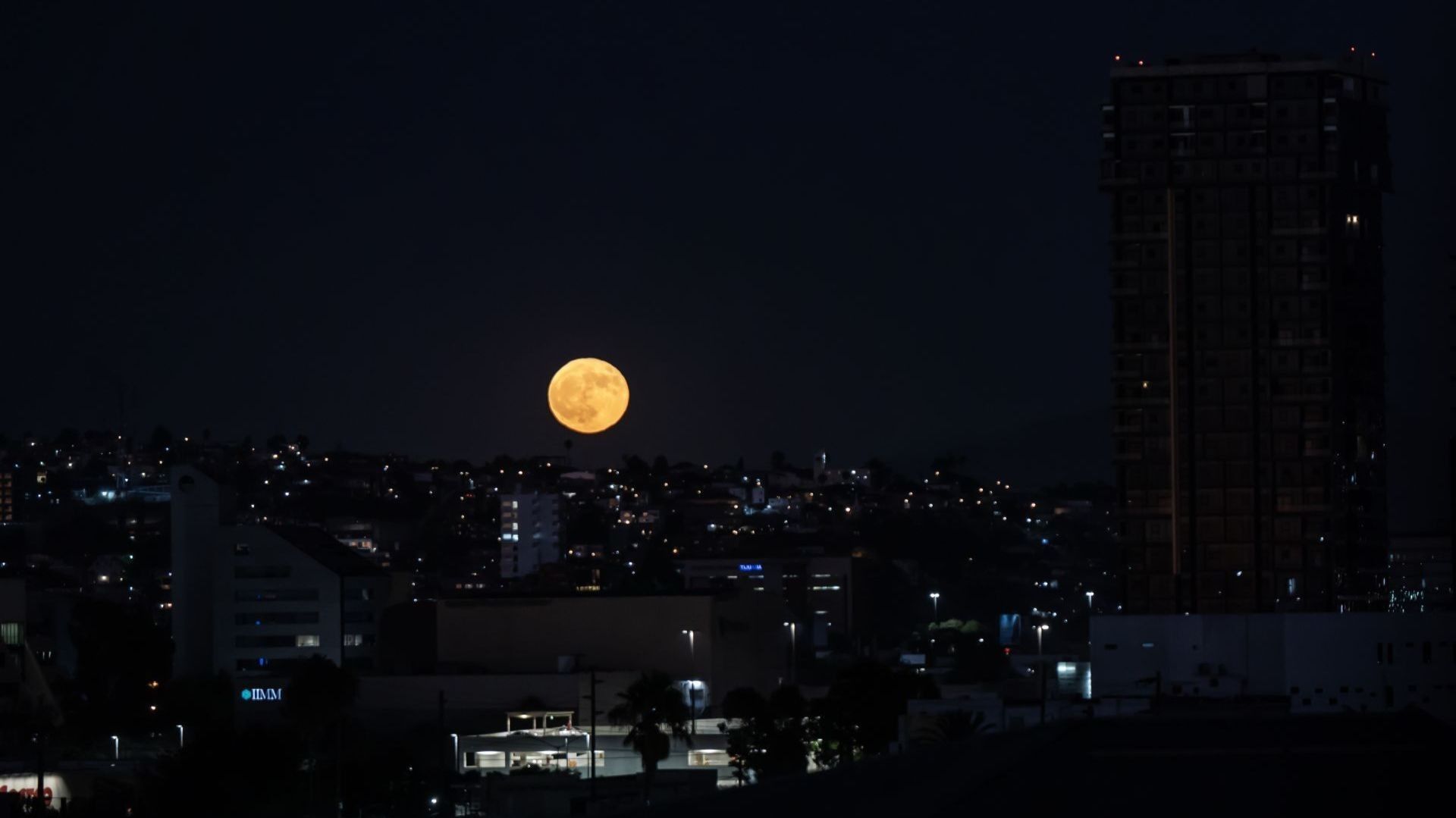 La superluna luce muy brillante en medio de un paisaje con edificios.