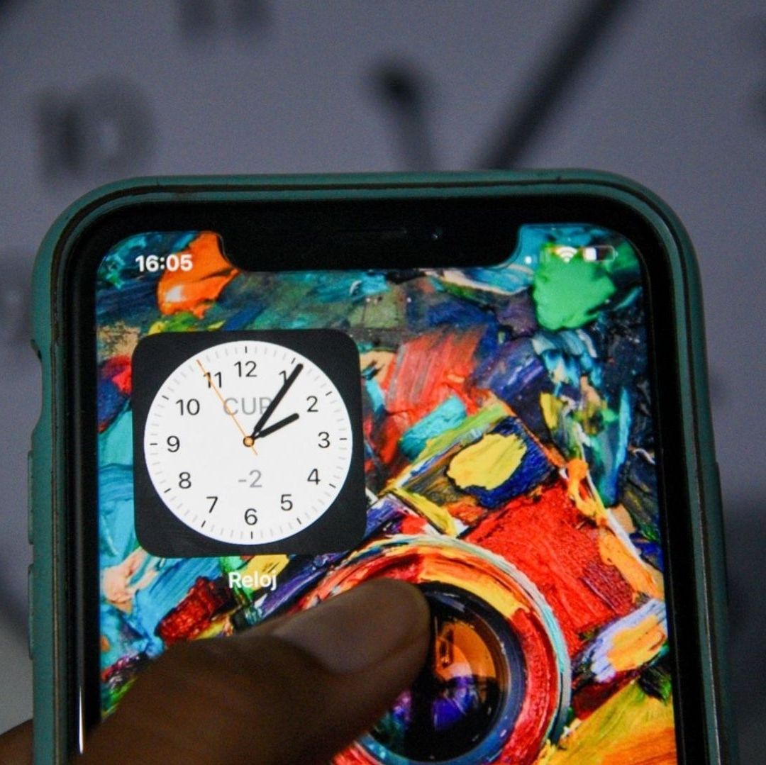 Una imagen de un celular que tiene de fondo un reloj.